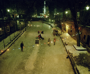 119758 Afbeelding van een bevroren Oudegracht te Utrecht, bij avond, met schaatsende mensen, vanaf de Jansbrug, uit het ...